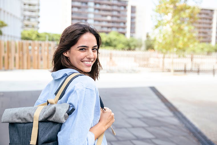 Happy student with backpack in the campus. Portrait of smiling woman looking at camera with bakcpack.